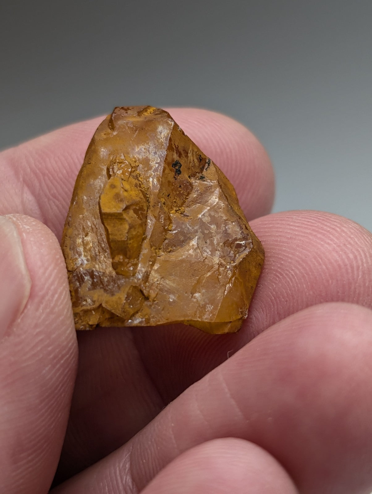 A translucent amber-colored piece of fossilized resin held in hand from set of 6 arkansas quartz crystals with natural iridescence