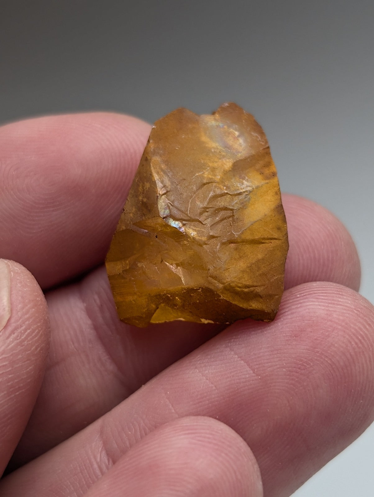 A hand holding a translucent amber arkansas quartz crystal with rough natural fractures and iridescence