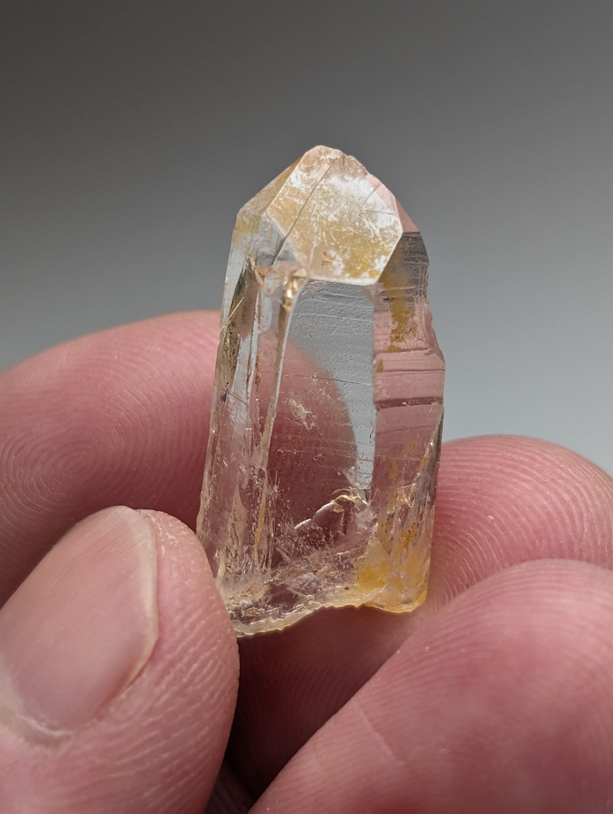 A translucent yellowish Arkansas quartz crystal with natural iridescence and visible inclusions held between fingers