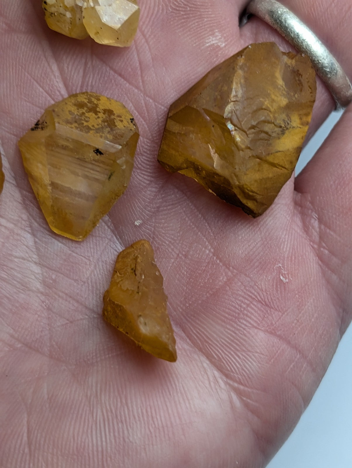 Set of 6 yellow amber-colored rough-cut arkansas quartz crystals with natural iridescence held in a hand