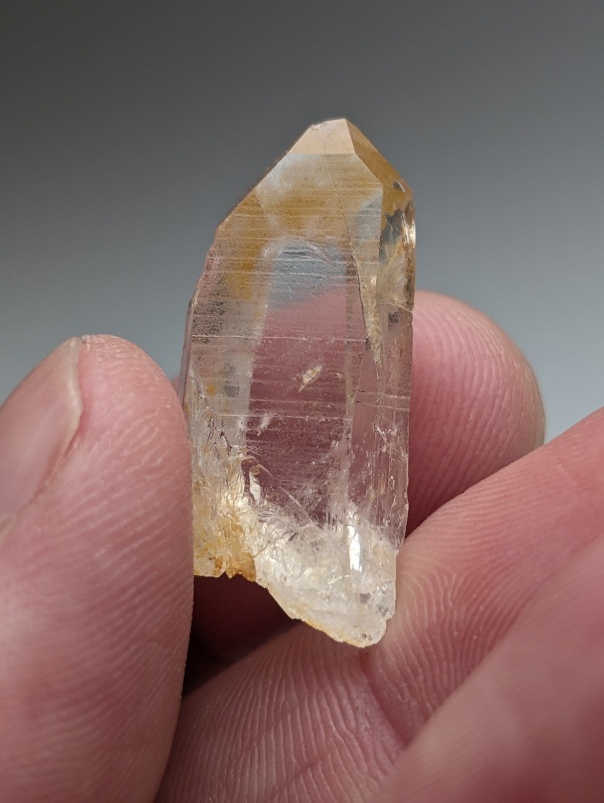 A translucent yellowish arkansas quartz crystal with natural iridescence and visible striations held between fingers