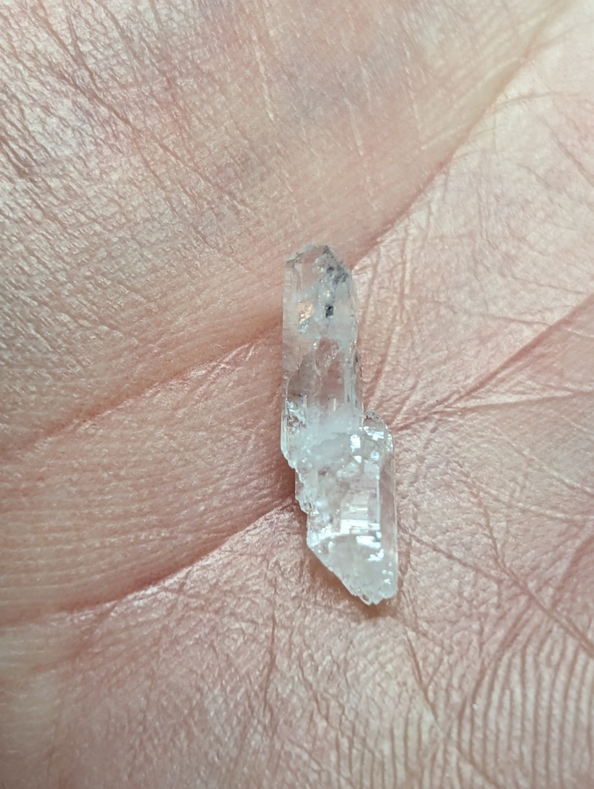 A translucent, clear quartz crystal with subtle internal inclusions and a pointed tip rests on an open palm.
