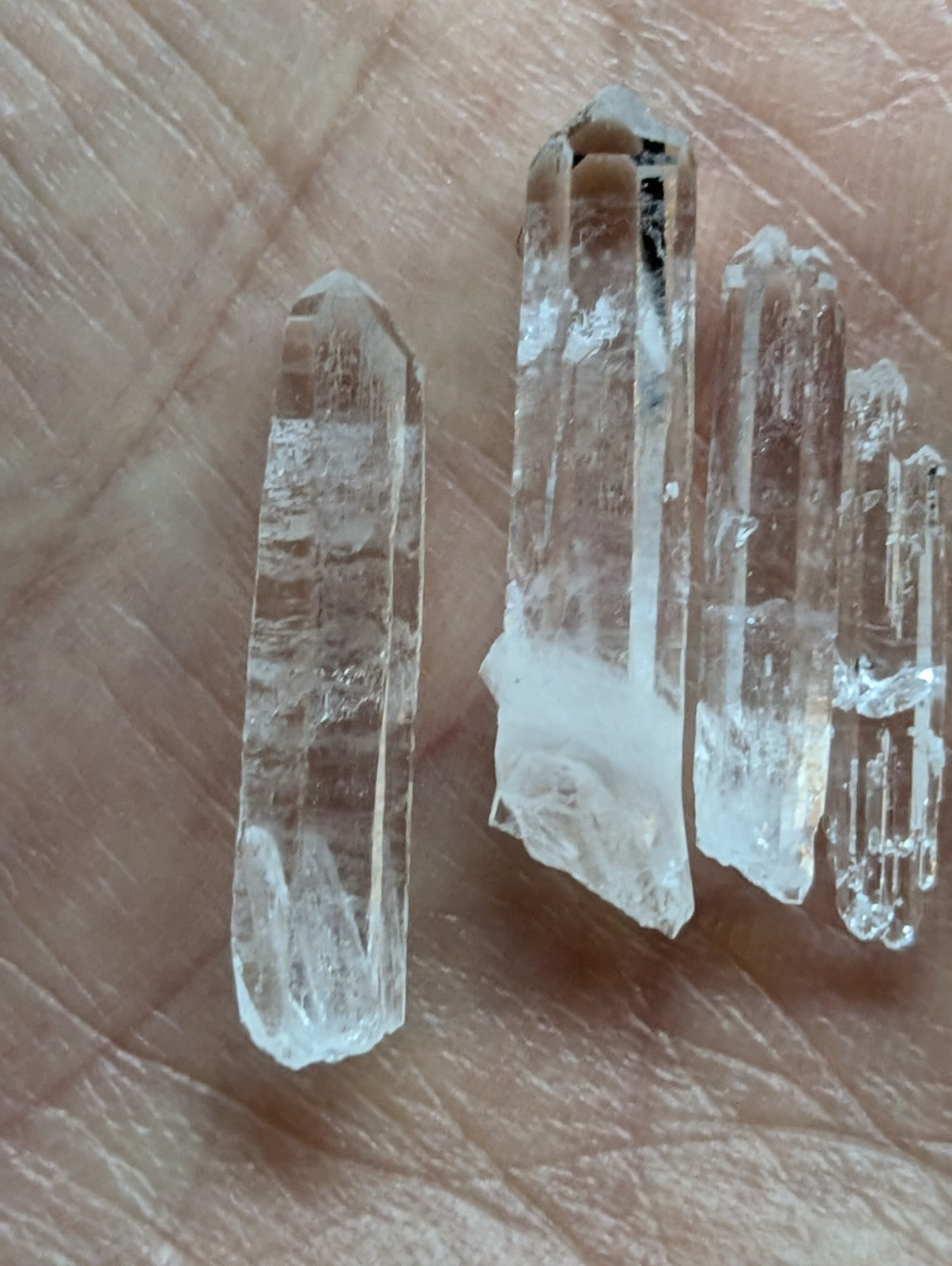 Clear quartz crystals with natural facets and internal inclusions, resting on a palm.