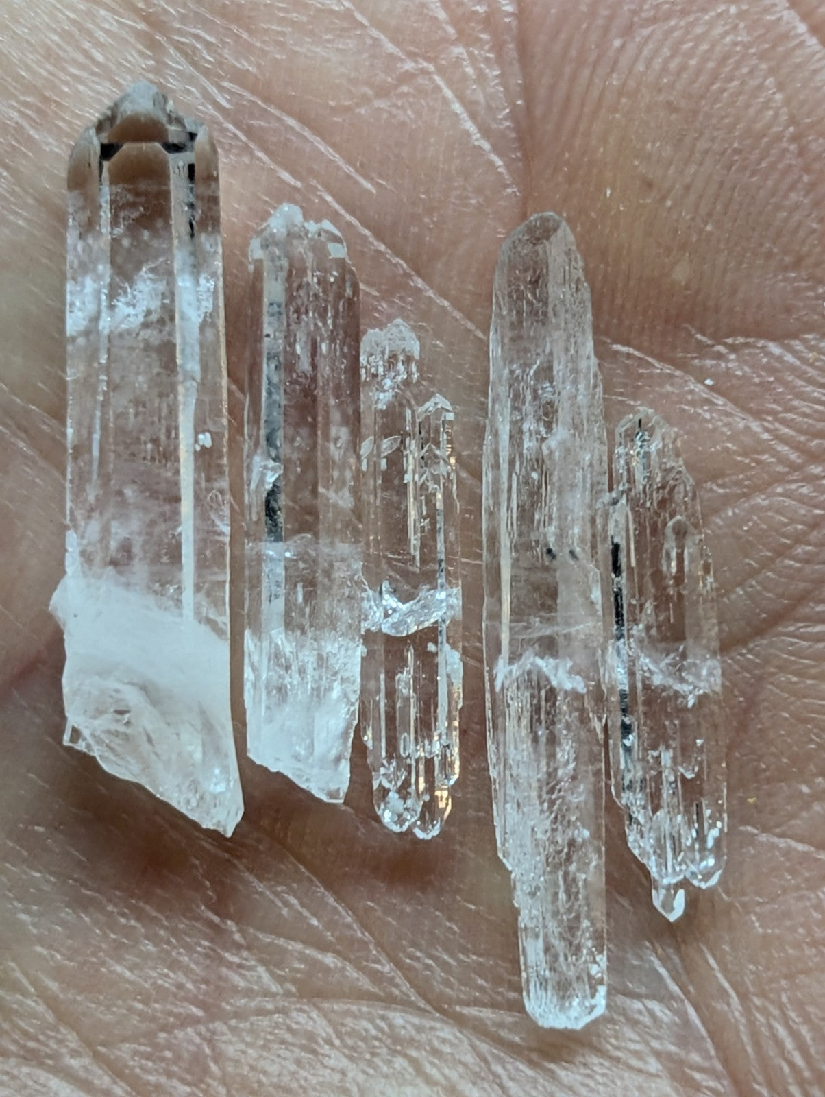 Clear quartz crystal points with natural facets and subtle internal inclusions, held gently in a palm.