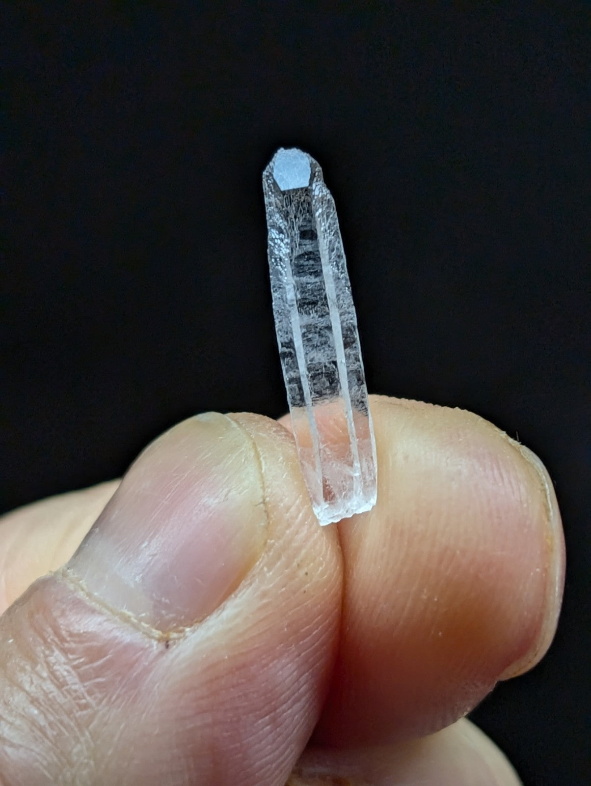 A clear quartz crystal with a faceted top and visible internal striations, held delicately between fingers.