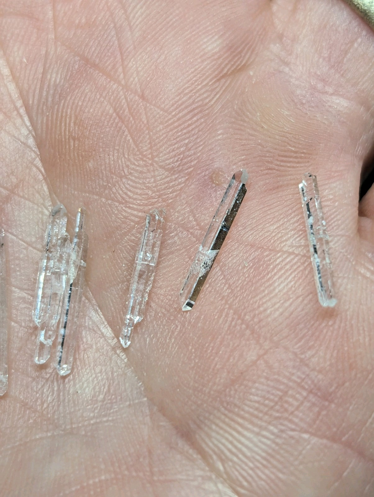 Clear quartz crystals with natural facets and subtle internal inclusions, resting on a palm.
