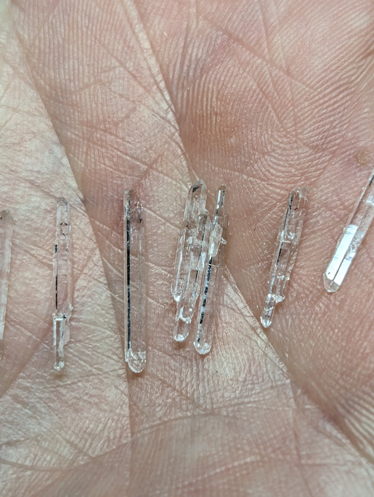 Clear quartz crystals with pointed tips and natural facets, resting on a palm.