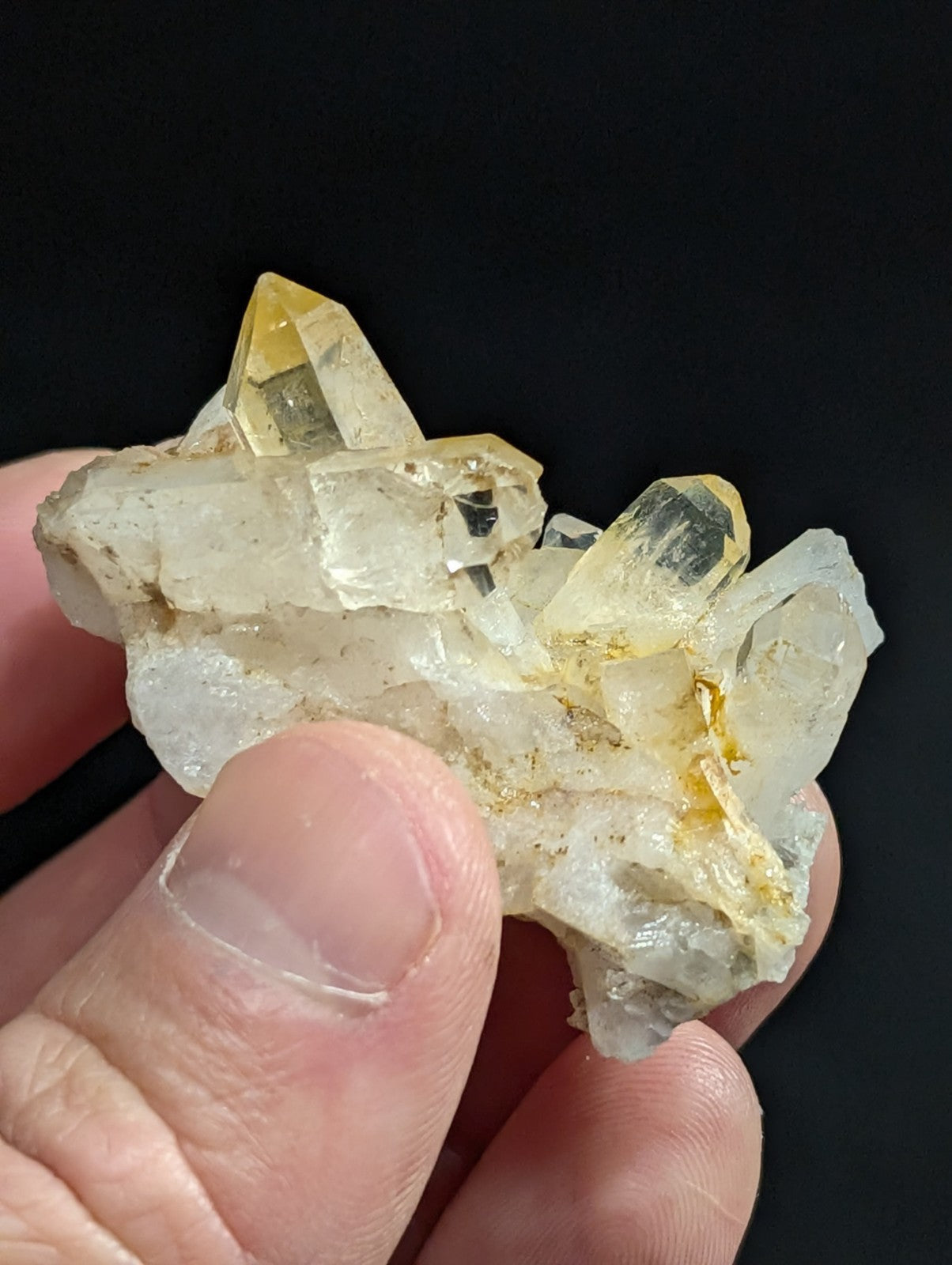 A cluster of translucent yellow and clear quartz crystals with sharp, pointed facets held in a hand.