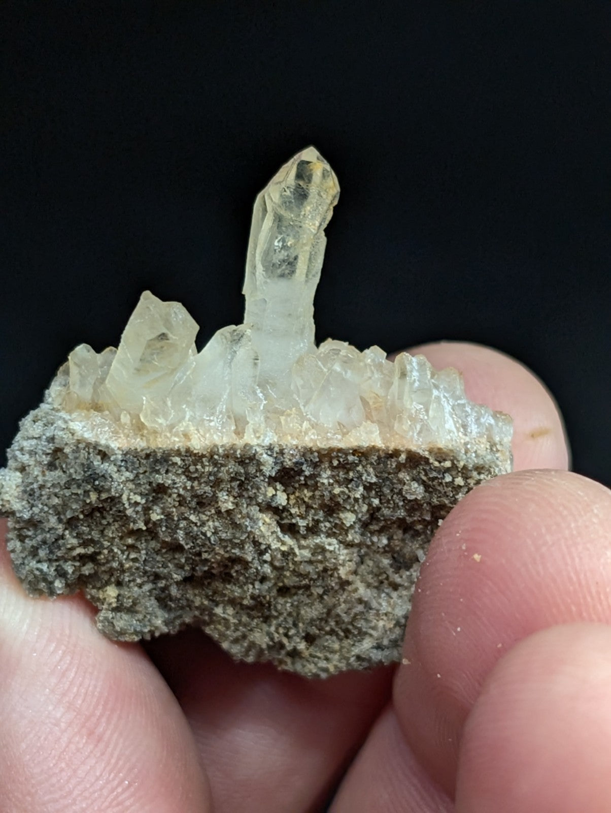 A translucent, pale yellow quartz crystal cluster emerging from a rough, grayish rock base.