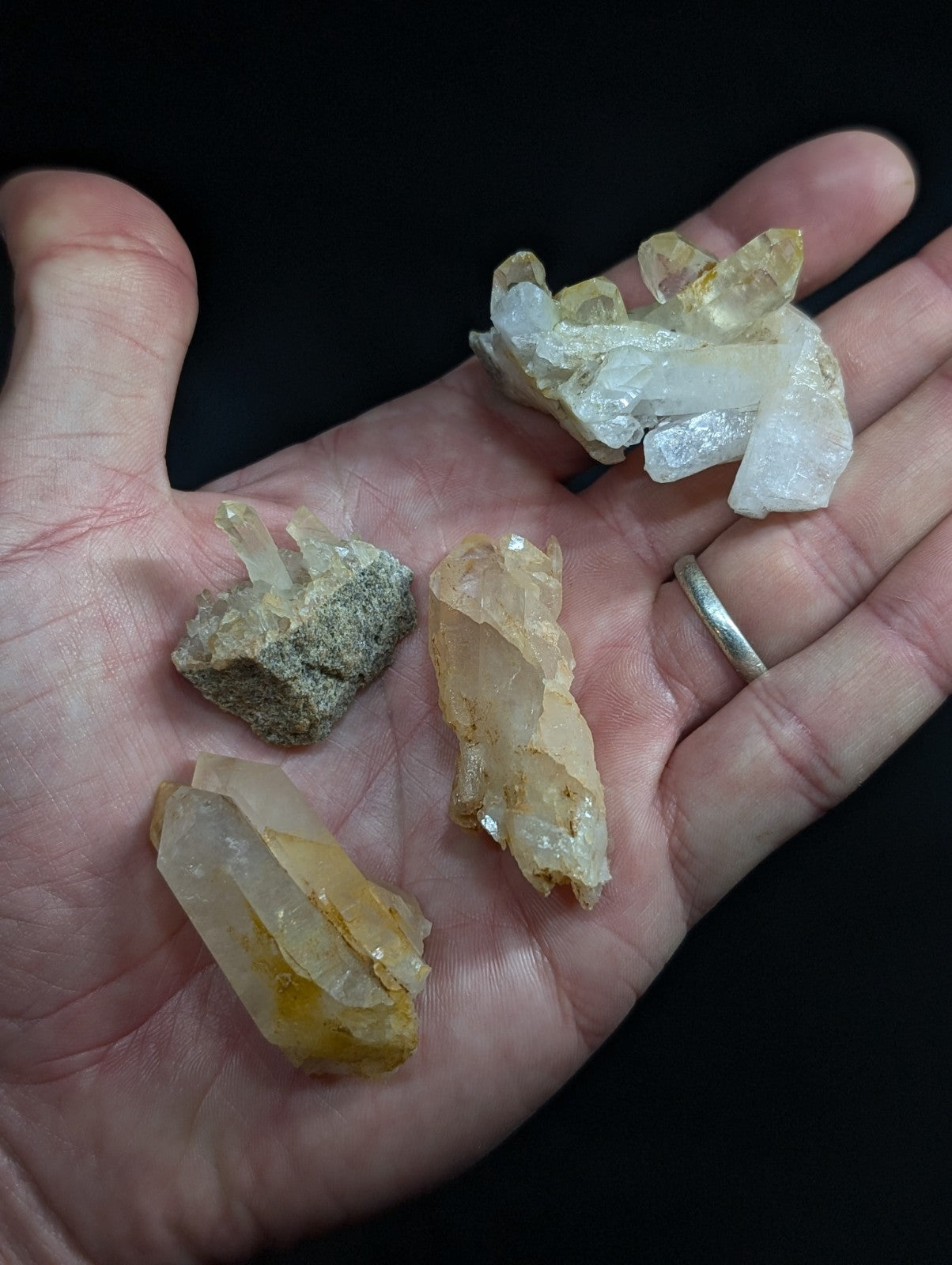 A hand holds several translucent yellow and white quartz crystals with pointed, faceted tips.