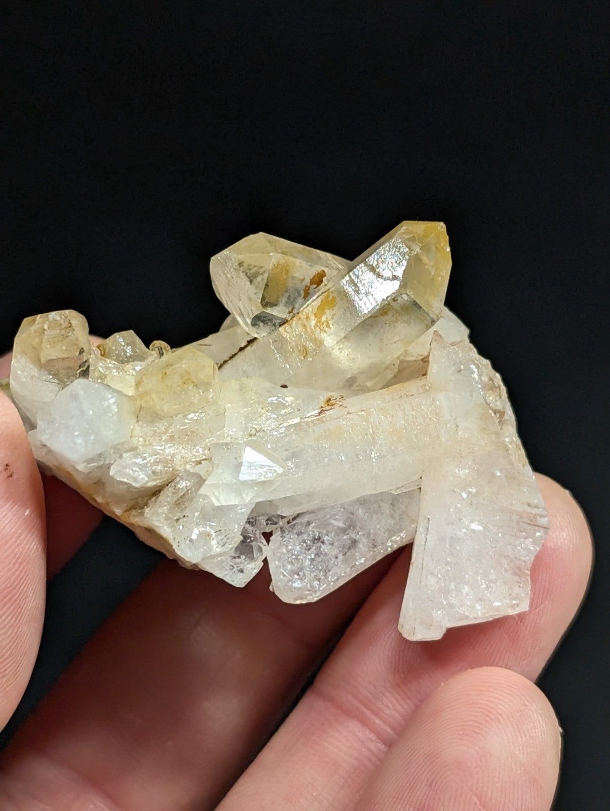 A cluster of translucent yellow and clear quartz crystals with sharp, faceted edges held in a hand.