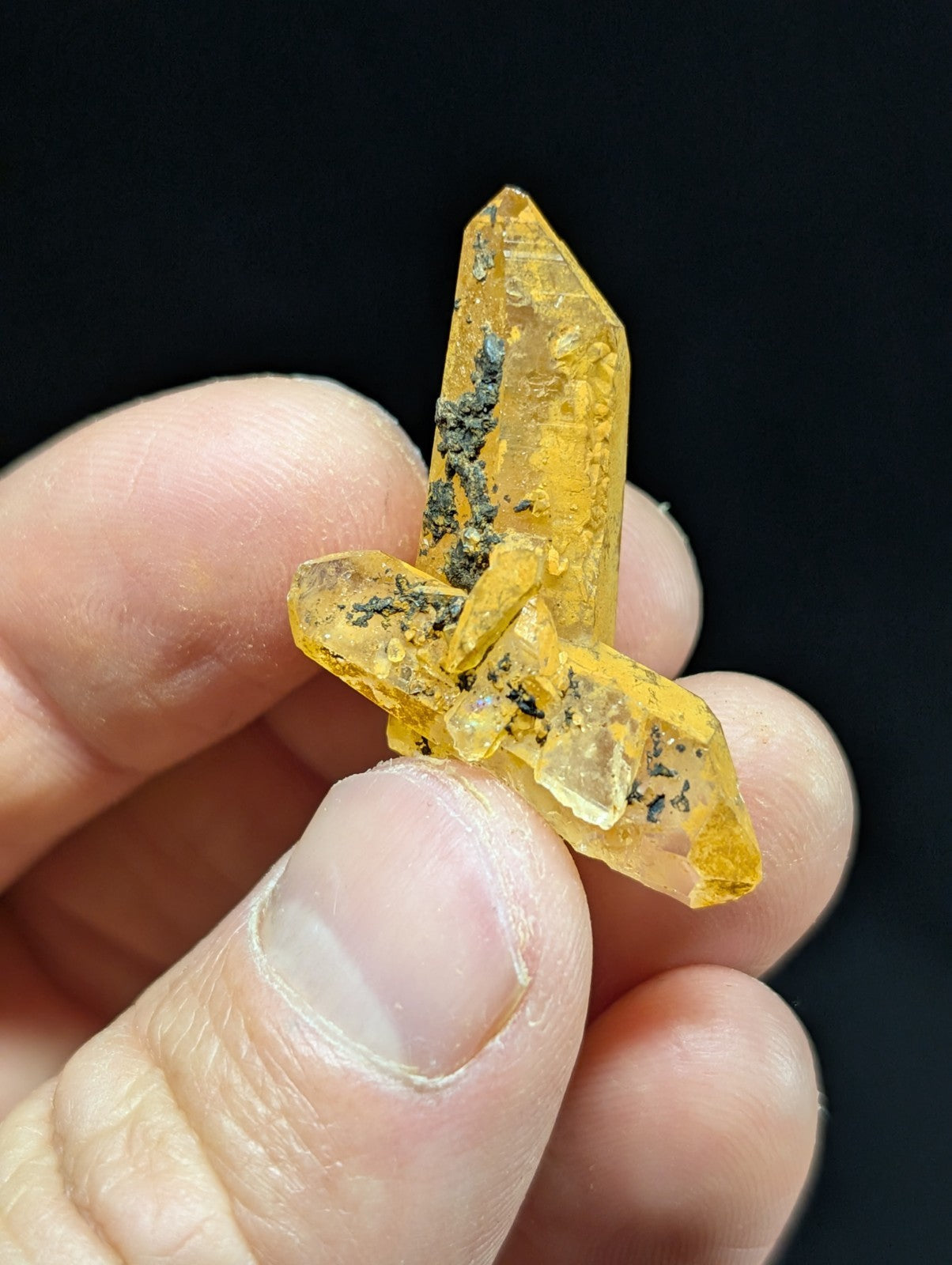 A translucent golden-yellow crystal cluster with sharp, angular facets and dark mineral inclusions.
