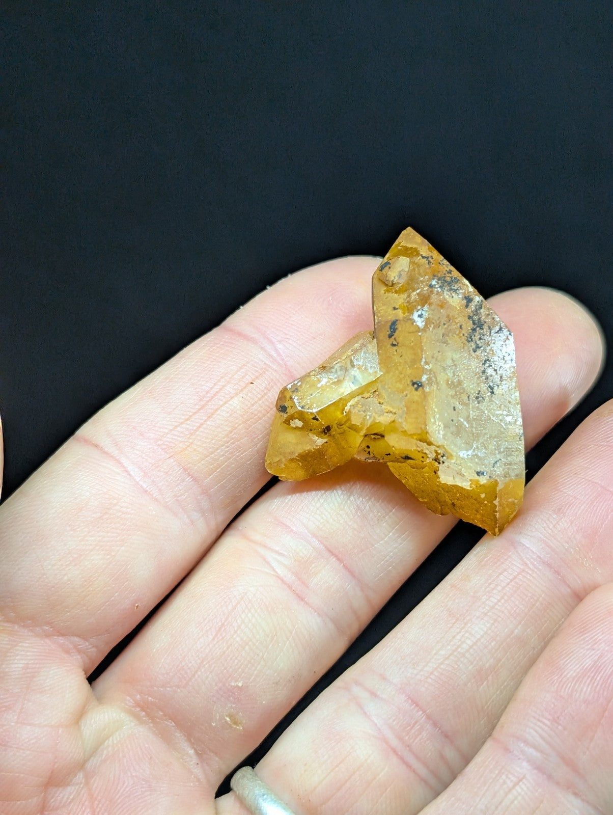 A translucent golden-yellow crystal cluster with natural facets and dark inclusions, held gently in a hand.