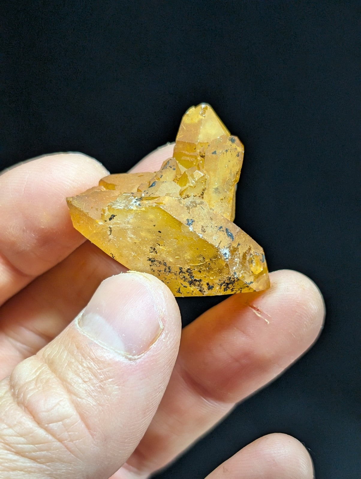 A translucent golden-yellow crystal cluster with sharp, angular facets and dark inclusions.