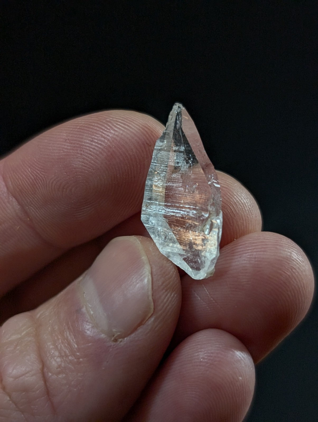 A clear, faceted quartz crystal with subtle internal striations and a pointed tip.