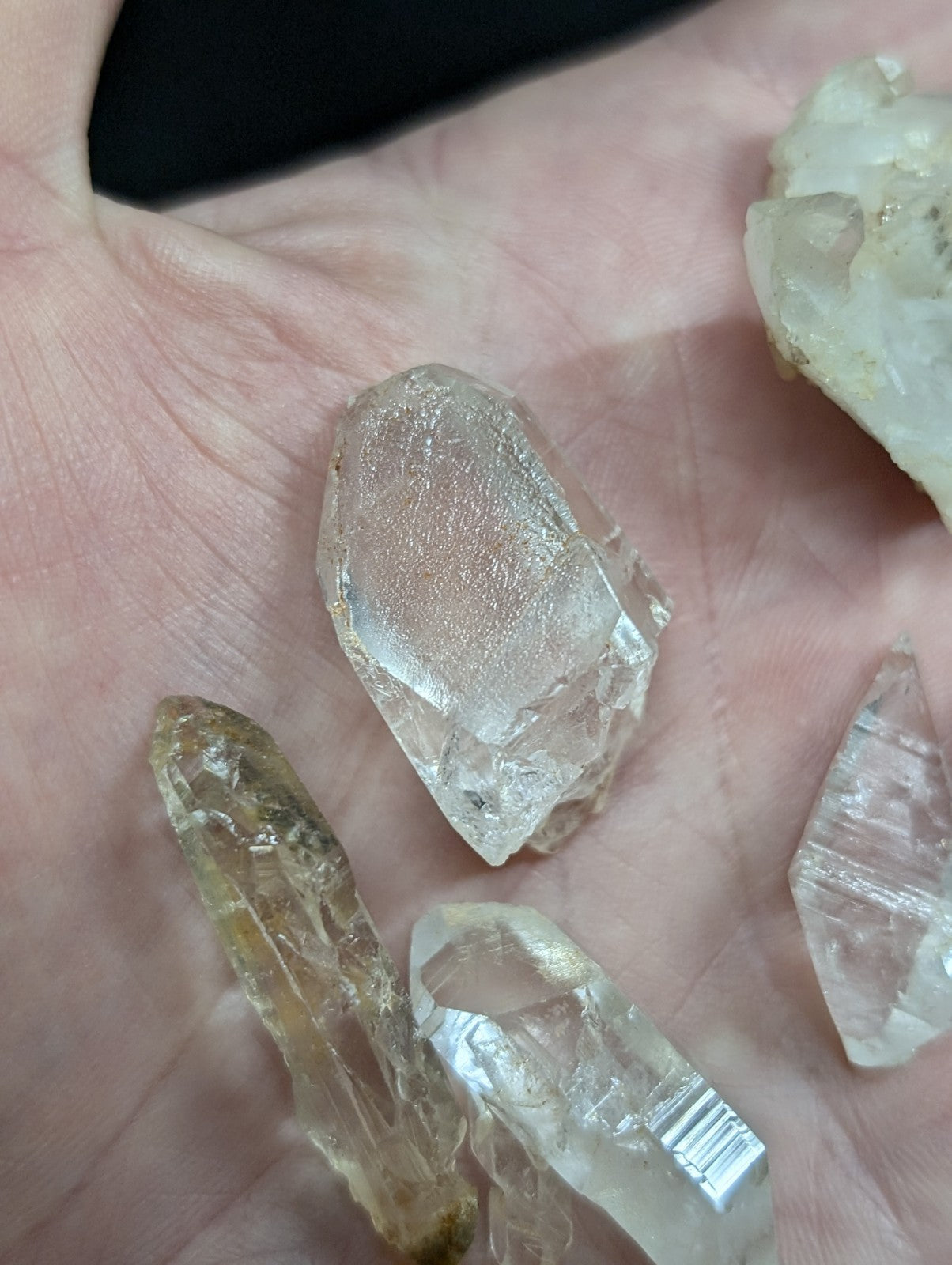 A translucent, faceted quartz crystal with a clear and slightly cloudy appearance rests in the palm of a hand.