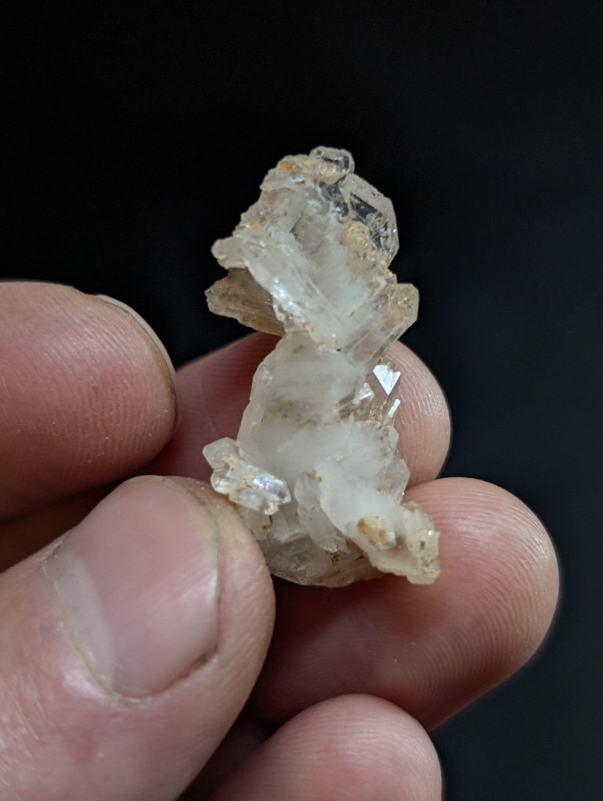 A translucent, crystalline quartz cluster with clear and slightly cloudy facets held between fingers.