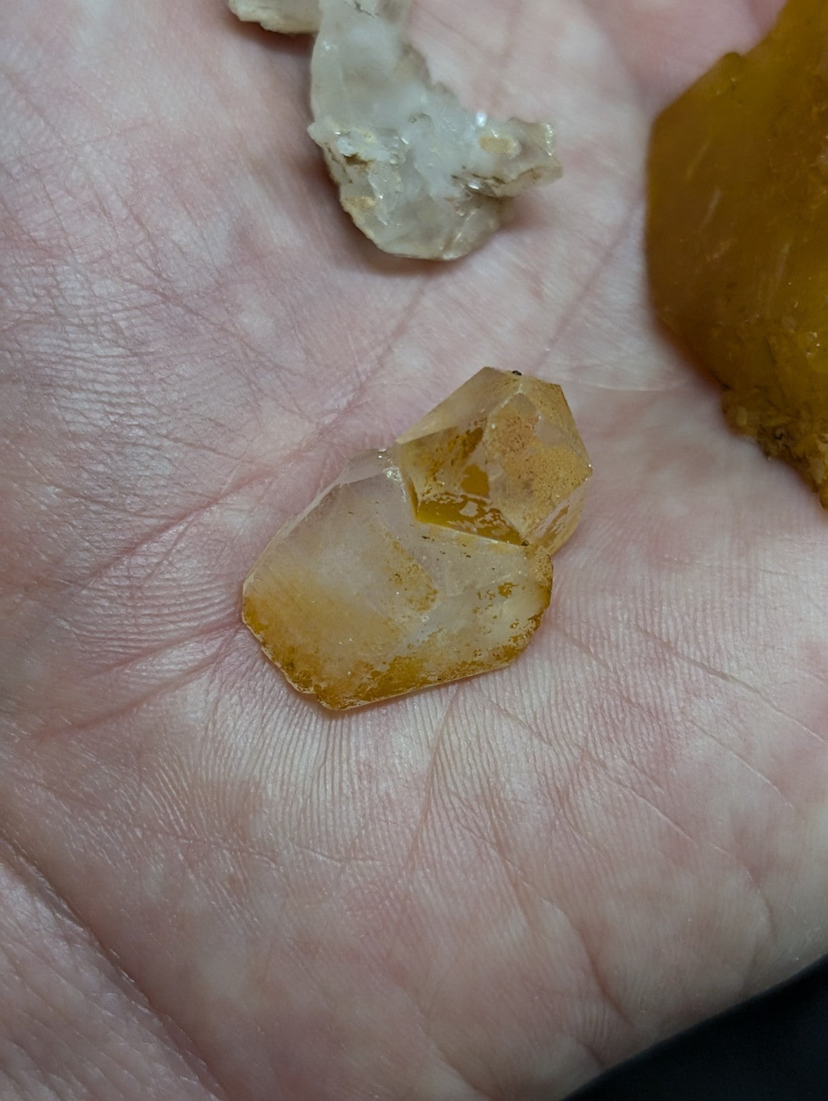 A translucent yellow-orange crystal with a faceted, geometric shape rests in the palm of a hand.