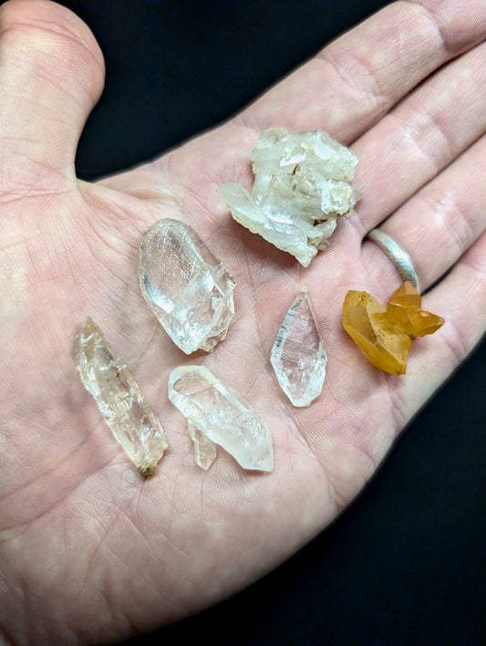 A hand holds a collection of clear and golden quartz crystals, each with distinct facets and natural formations.