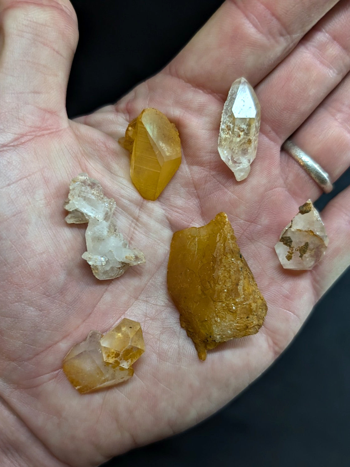 A hand holds a collection of natural quartz crystals, featuring transparent and golden-yellow specimens with varied facets and rough textures.