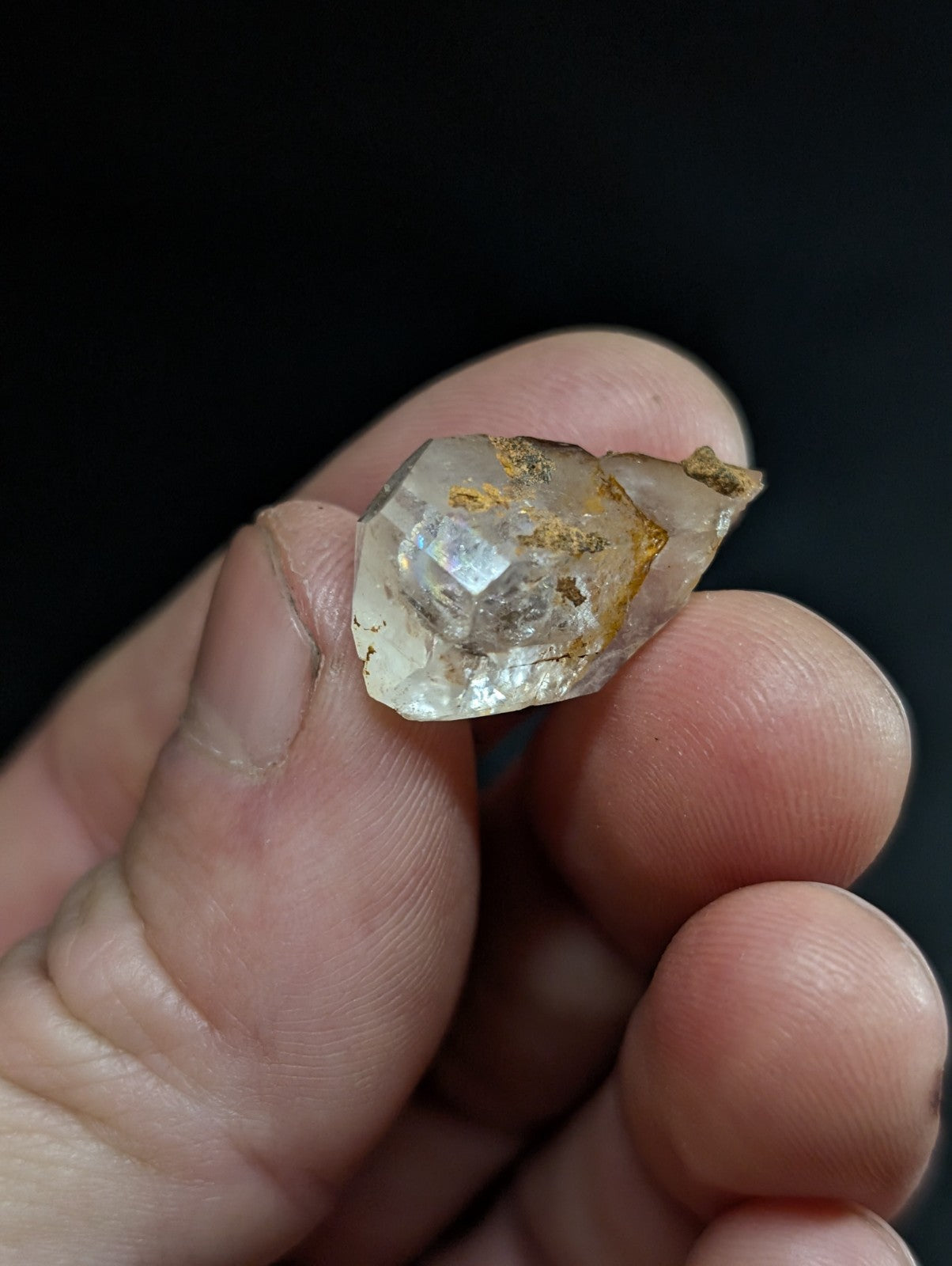 A translucent, faceted quartz crystal with golden mineral inclusions held gently between fingers.