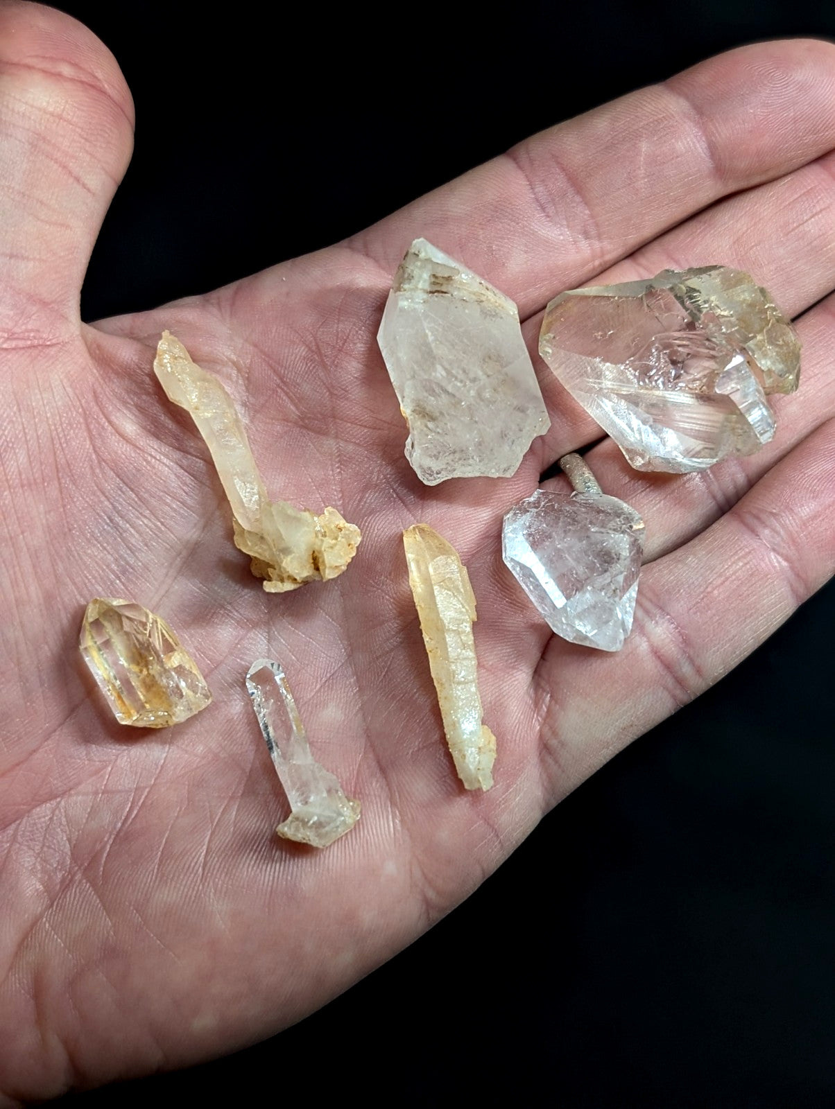 A hand holds a collection of clear and yellowish quartz crystals, each with distinct facets and natural formations.