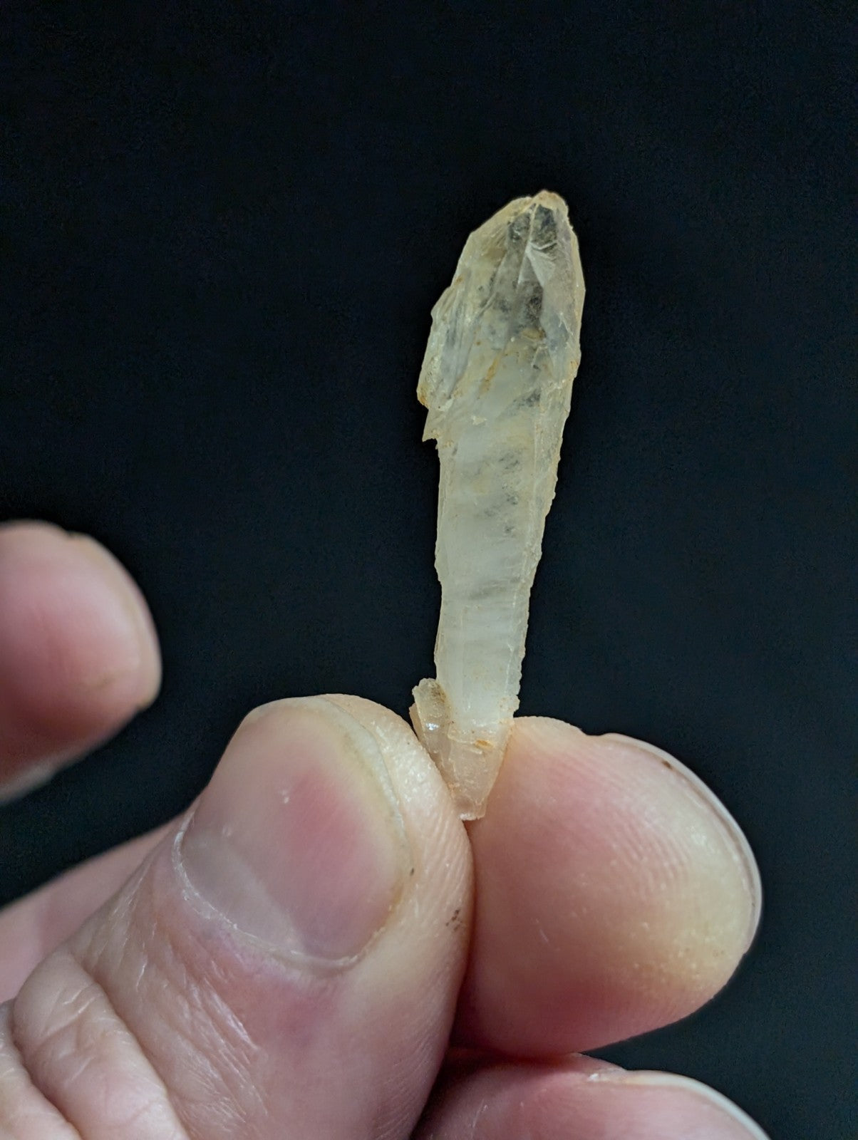 A translucent, pale yellow crystal with a pointed tip and visible internal striations.