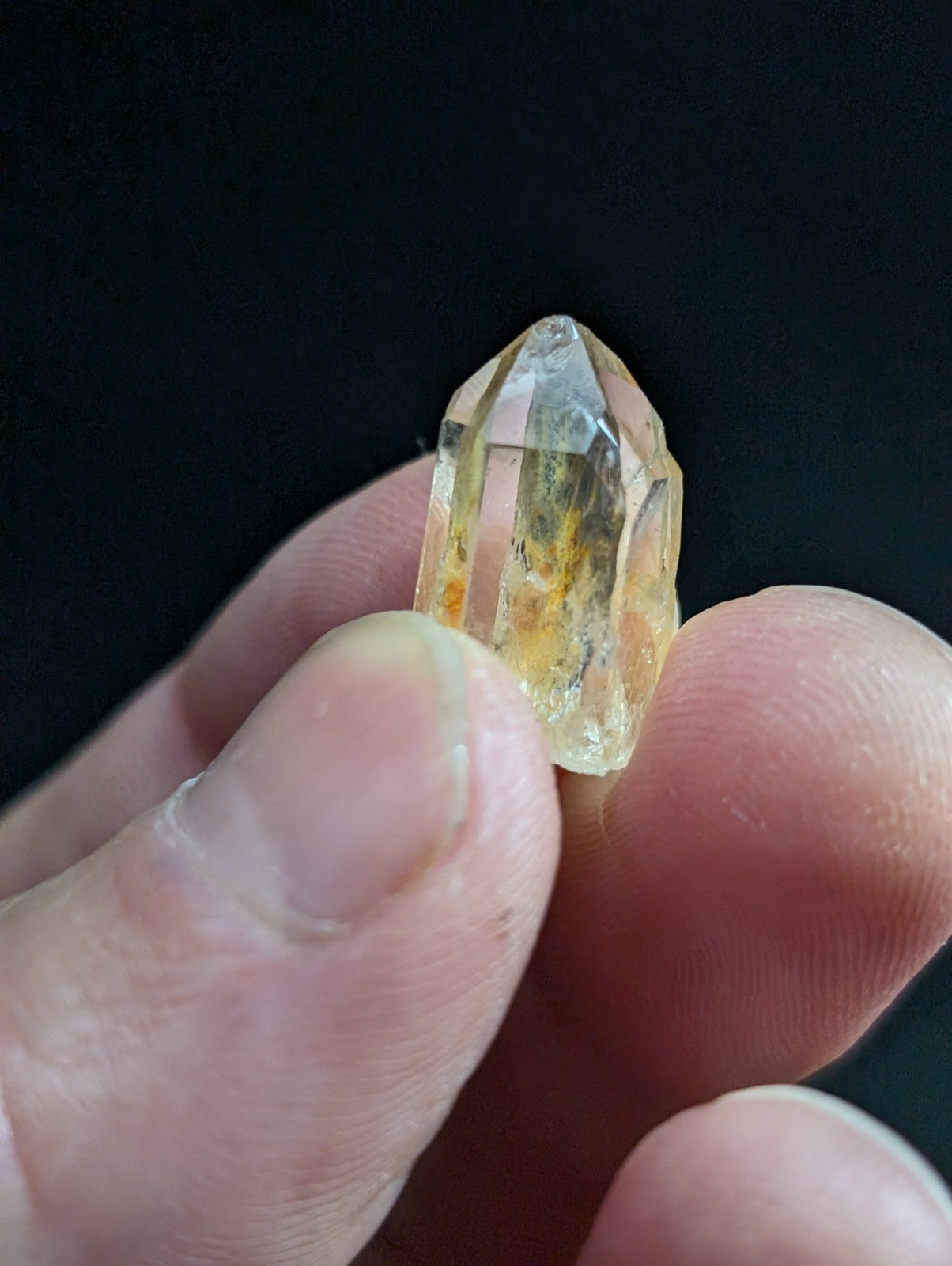 A translucent yellowish quartz crystal with a pointed tip and visible internal inclusions, held gently between fingers.