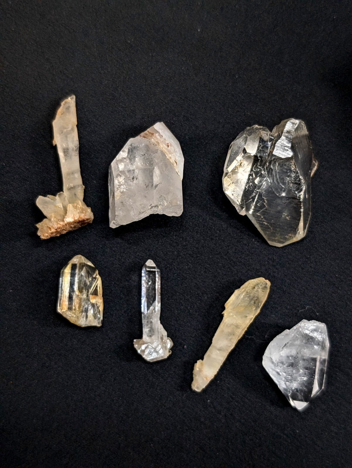 Clear quartz crystals of varying sizes and shapes, some with golden inclusions or earthy bases.