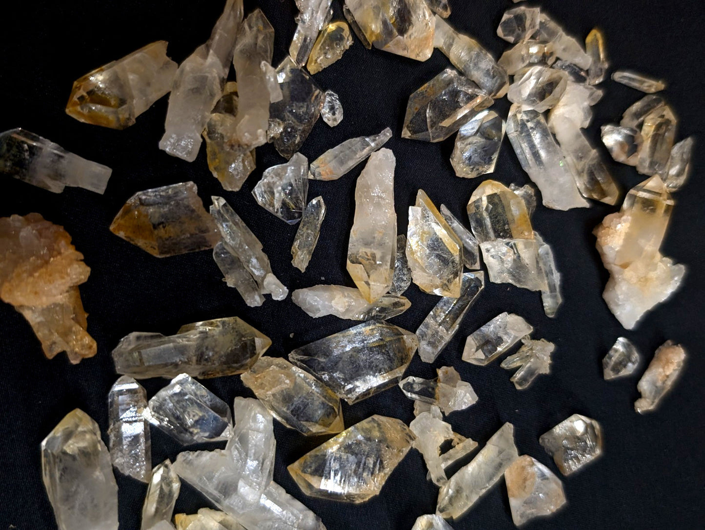 Clear and golden-yellow quartz crystals with sharp, faceted edges scattered across a dark surface.