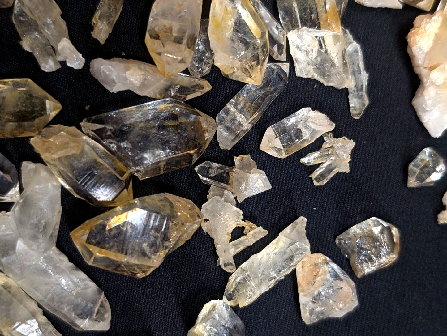 Clear and golden-yellow quartz crystals with faceted, geometric shapes scattered across a dark surface.