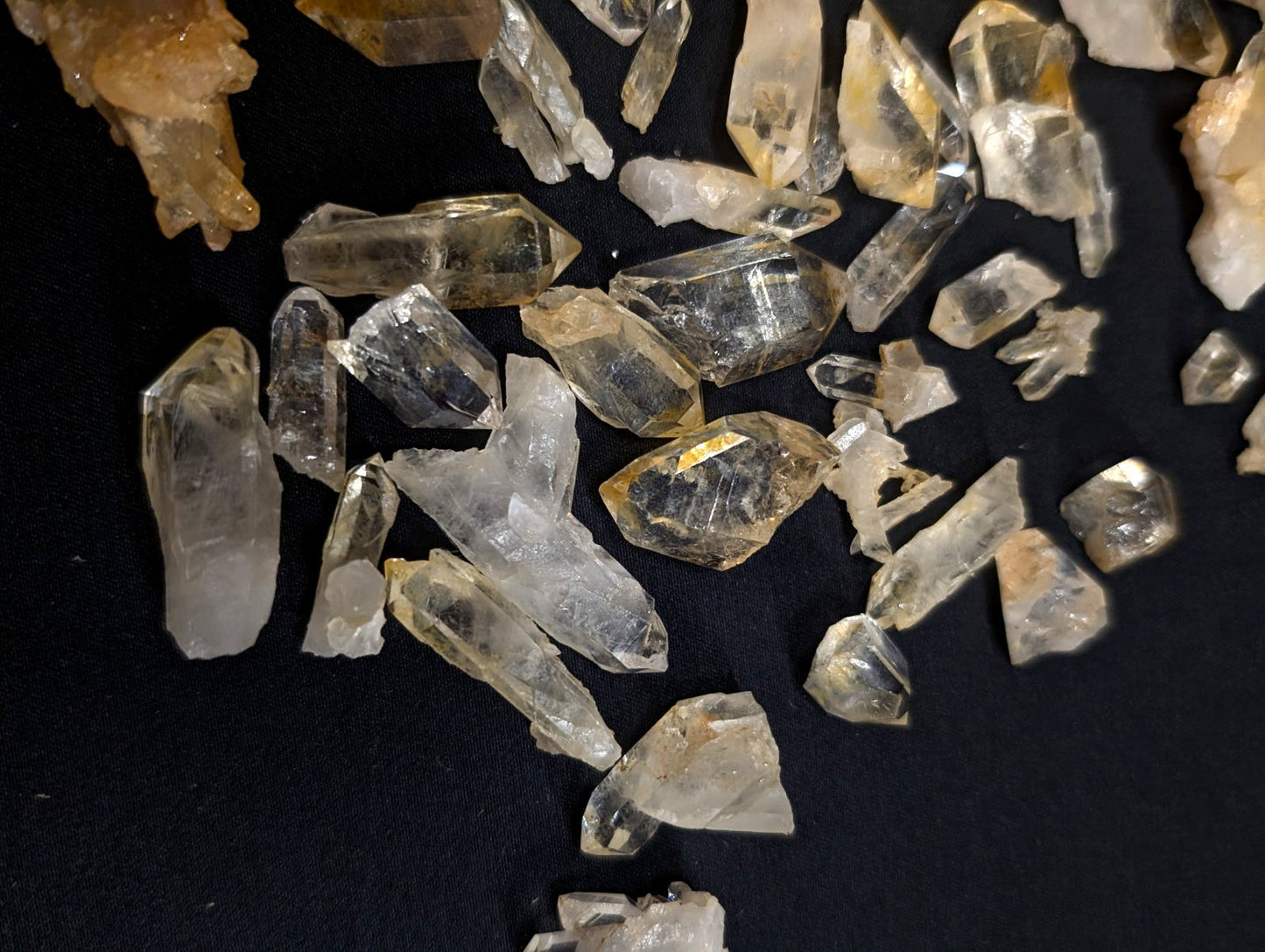 Clear and golden-yellow quartz crystals with pointed, faceted tips scattered across a dark surface.