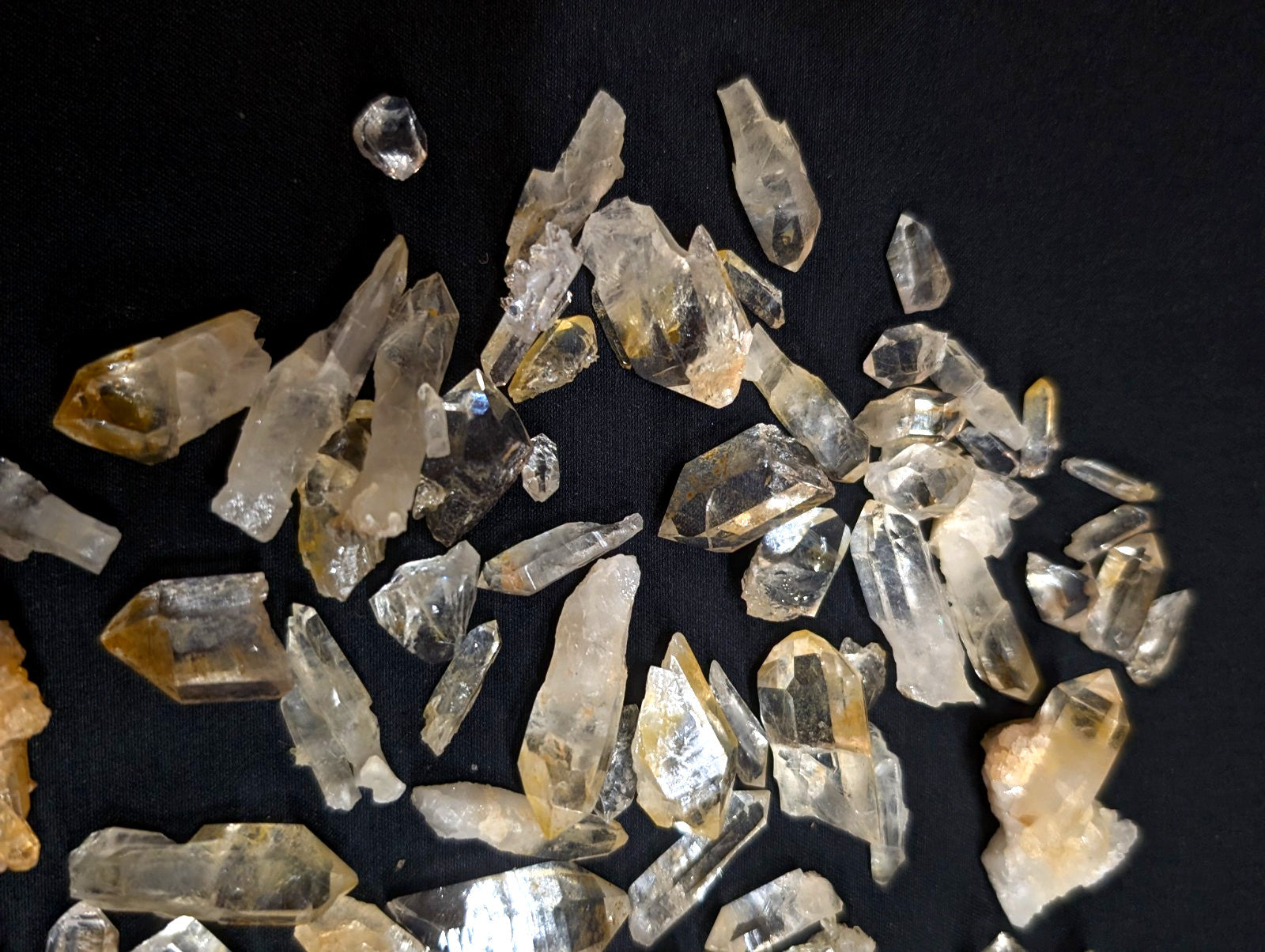 Clear and golden-yellow quartz crystals with pointed, faceted shapes scattered across a dark surface.
