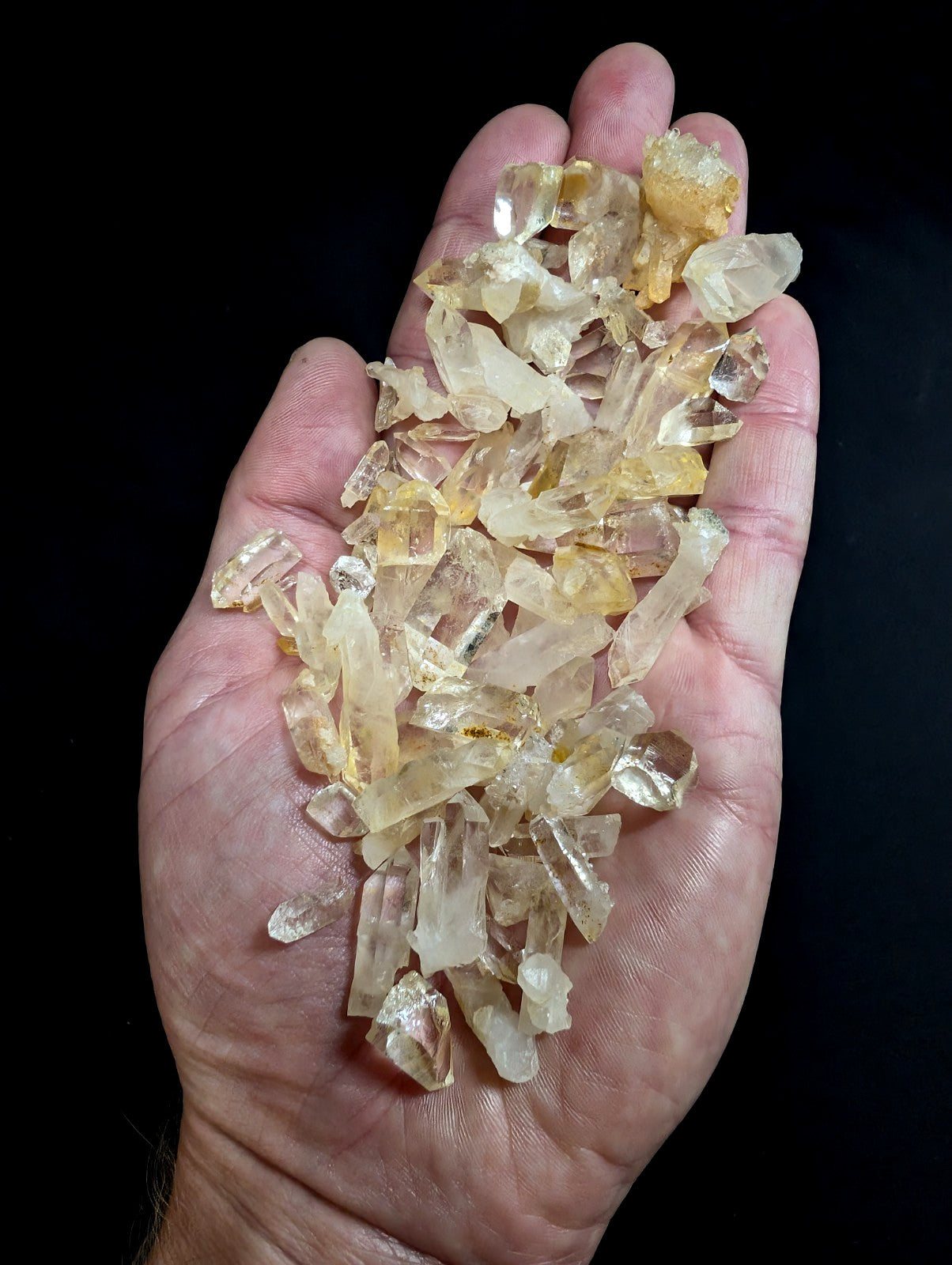 A hand holds a collection of translucent yellow and clear quartz crystals with jagged, faceted edges.