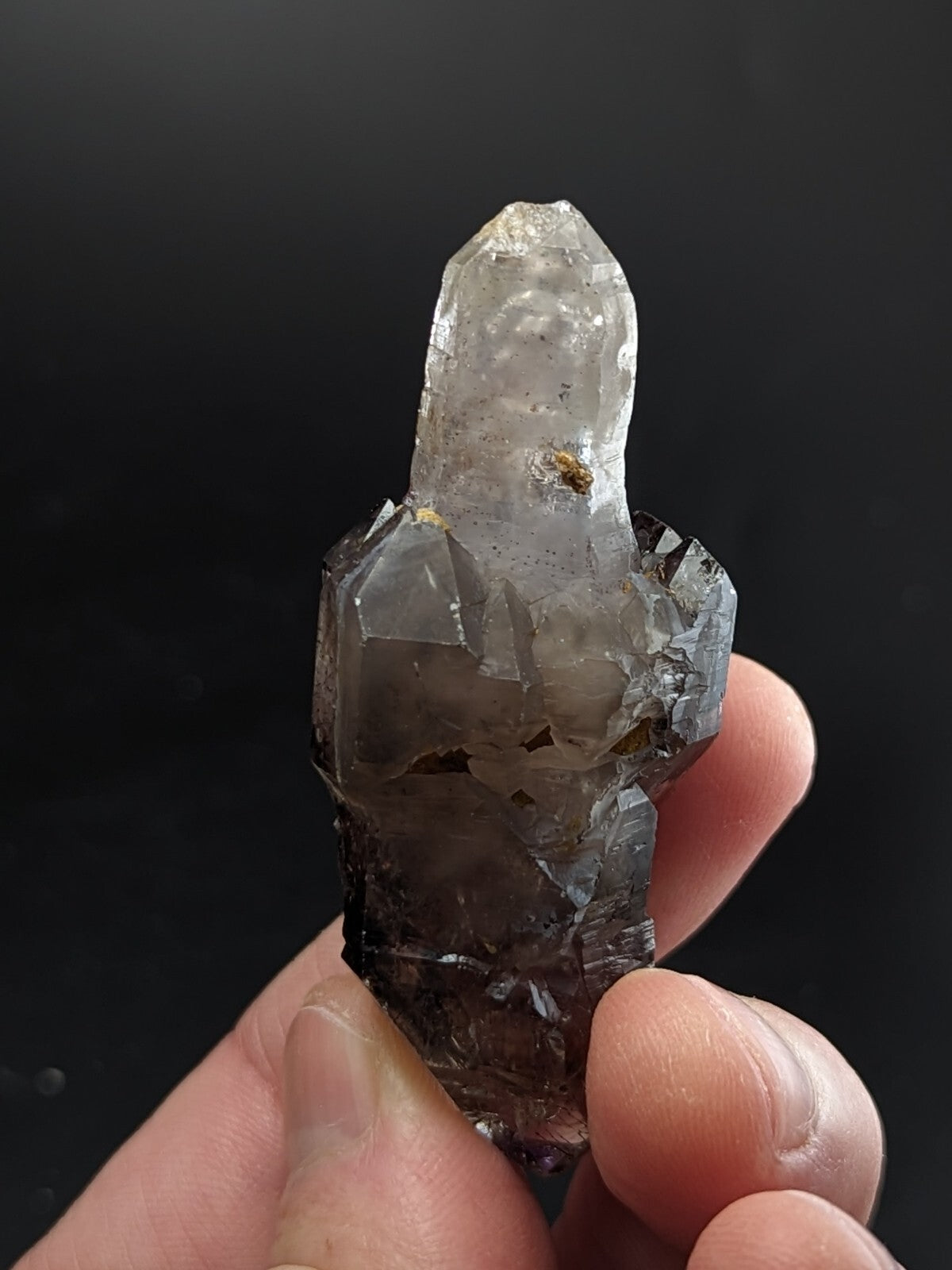 A translucent smoky quartz crystal cluster with a pointed, clear tip and darker, faceted base held in hand.