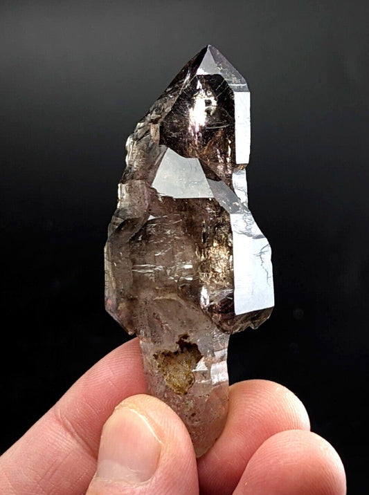 A translucent smoky quartz crystal with a pointed tip and visible internal inclusions, held gently between fingers.