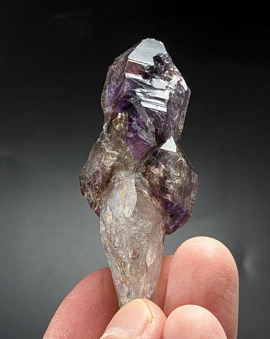 A hand holds a natural amethyst crystal cluster with translucent purple and clear quartz formations.