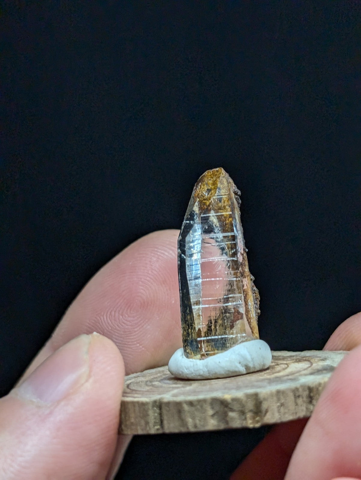 A translucent, amber-hued crystal with visible internal striations and a rough, earthy base.