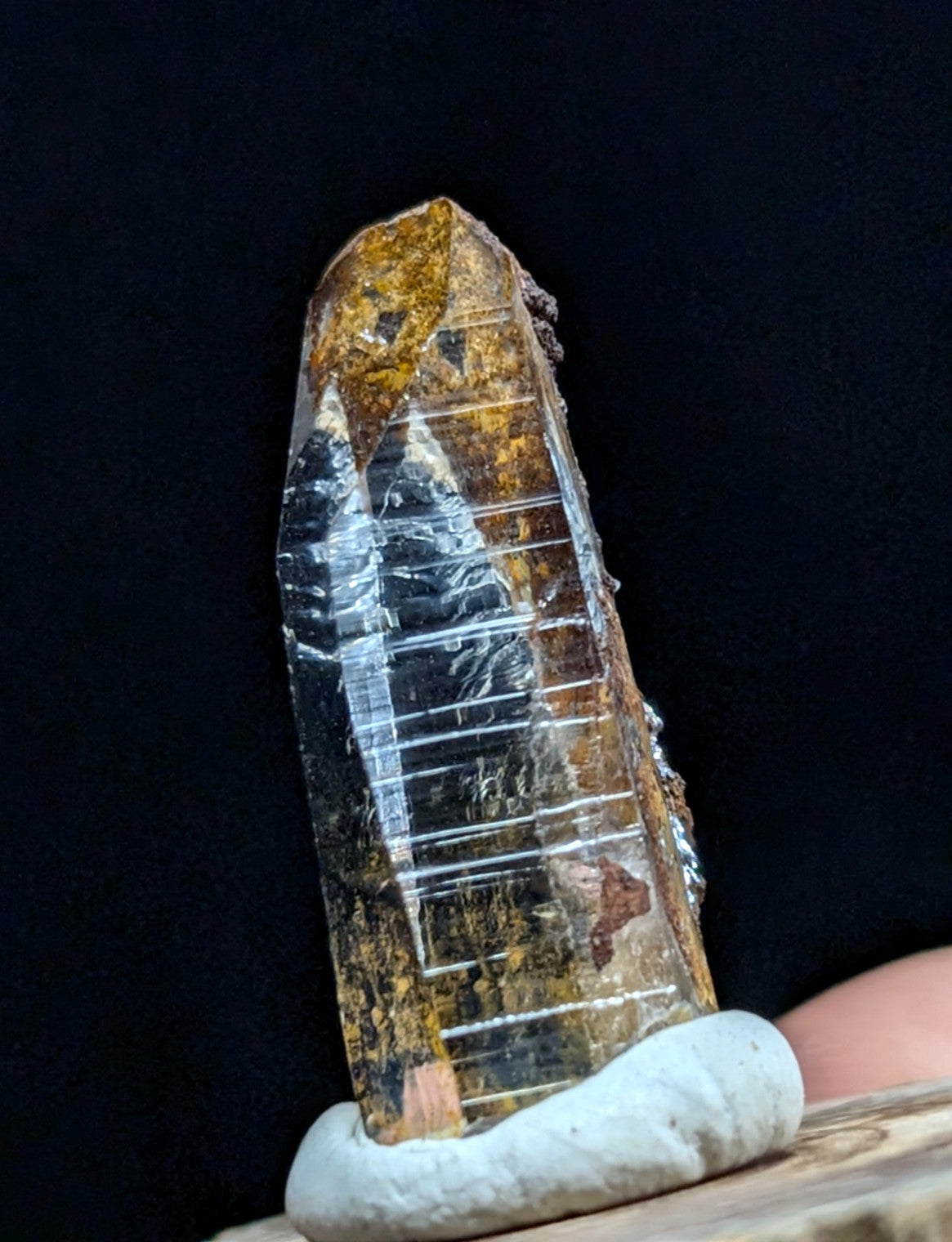 A translucent, amber-hued crystal with visible internal striations and earthy mineral inclusions rests on a white ceramic display stand.