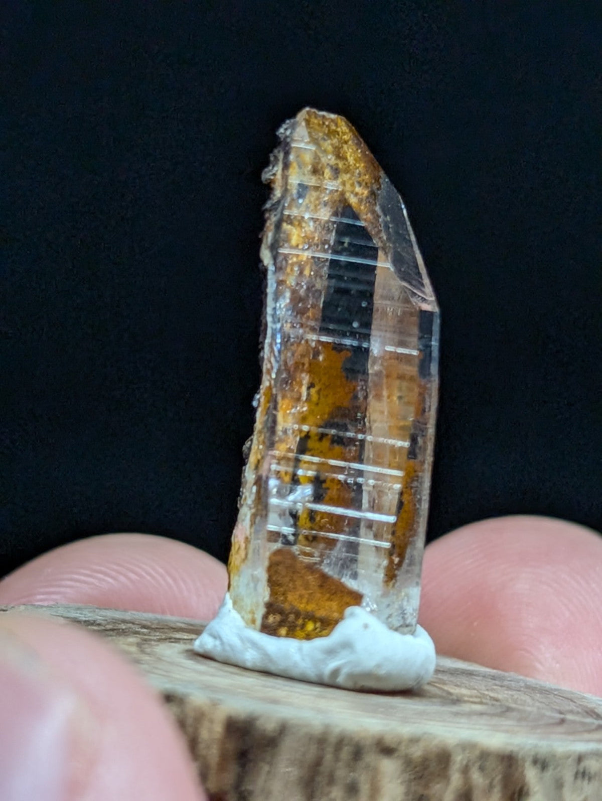 A translucent amber-hued crystal with visible internal striations and a rough, earthy base.