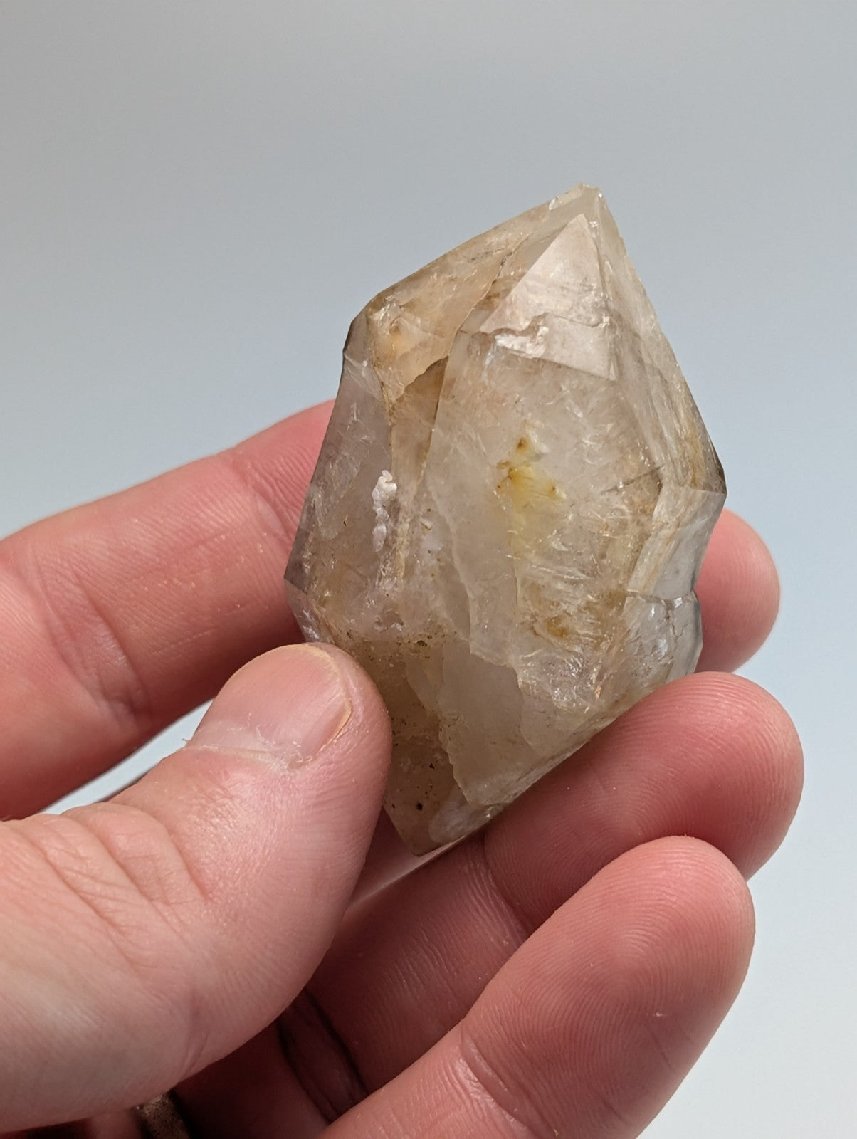 A translucent, pale yellowish quartz crystal with a pointed tip and visible internal inclusions.