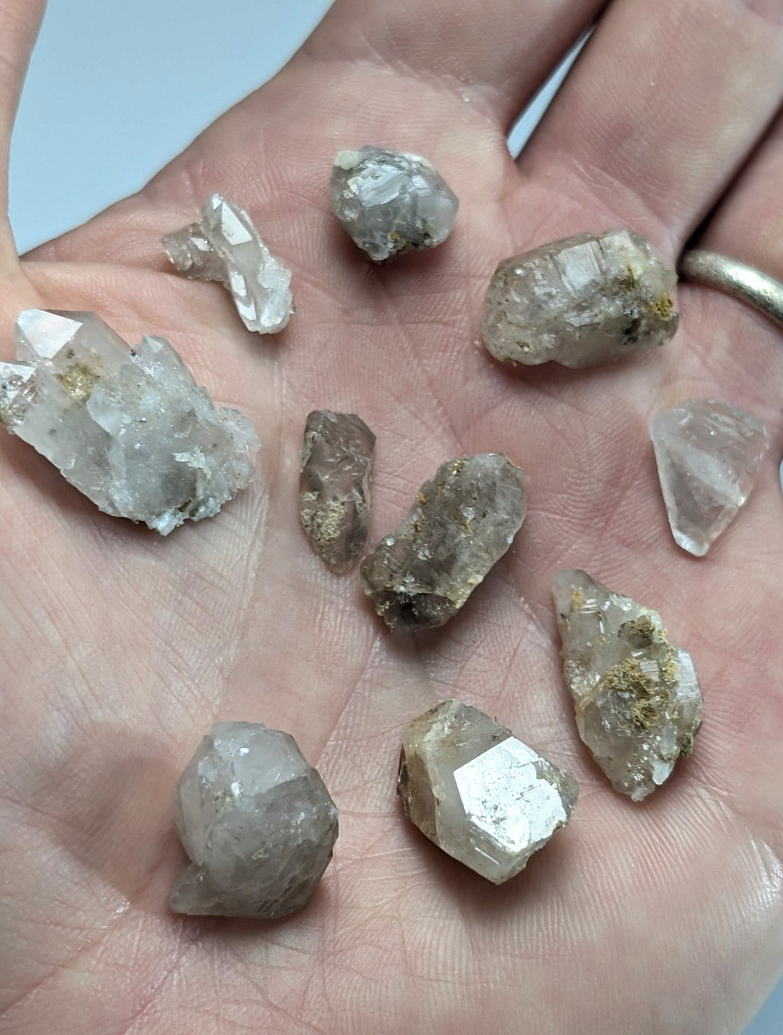 A hand holds a collection of raw, translucent quartz crystals with natural facets and earthy mineral inclusions.