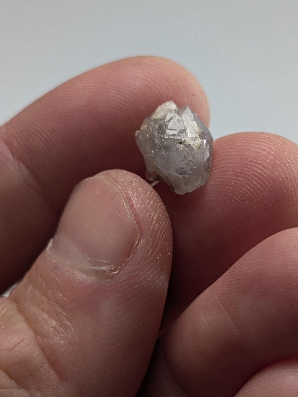 A raw, faceted diamond held between fingers.