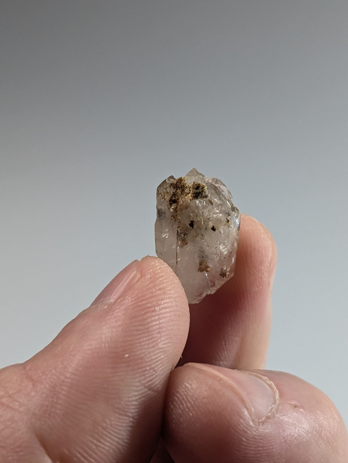 A translucent, rough-hewn quartz crystal with embedded dark inclusions.