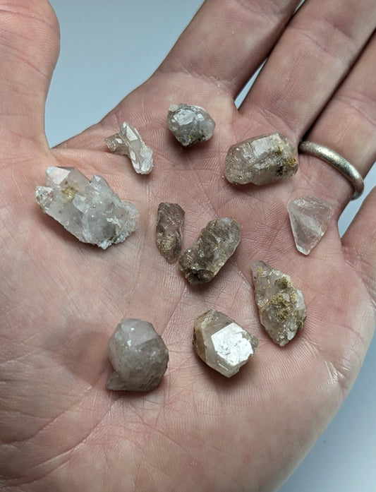 A hand holds a collection of raw, translucent quartz crystals with varying sizes and earthy tones.