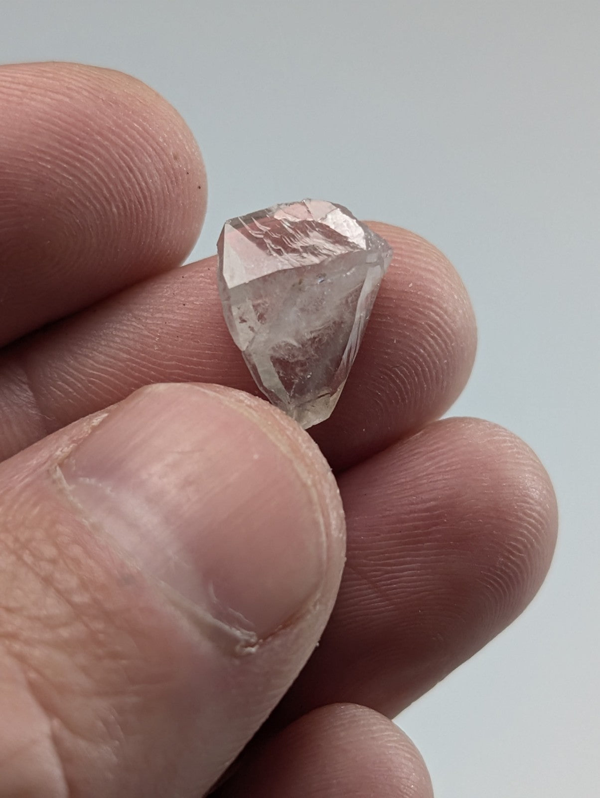 A clear, faceted raw diamond held between fingers.