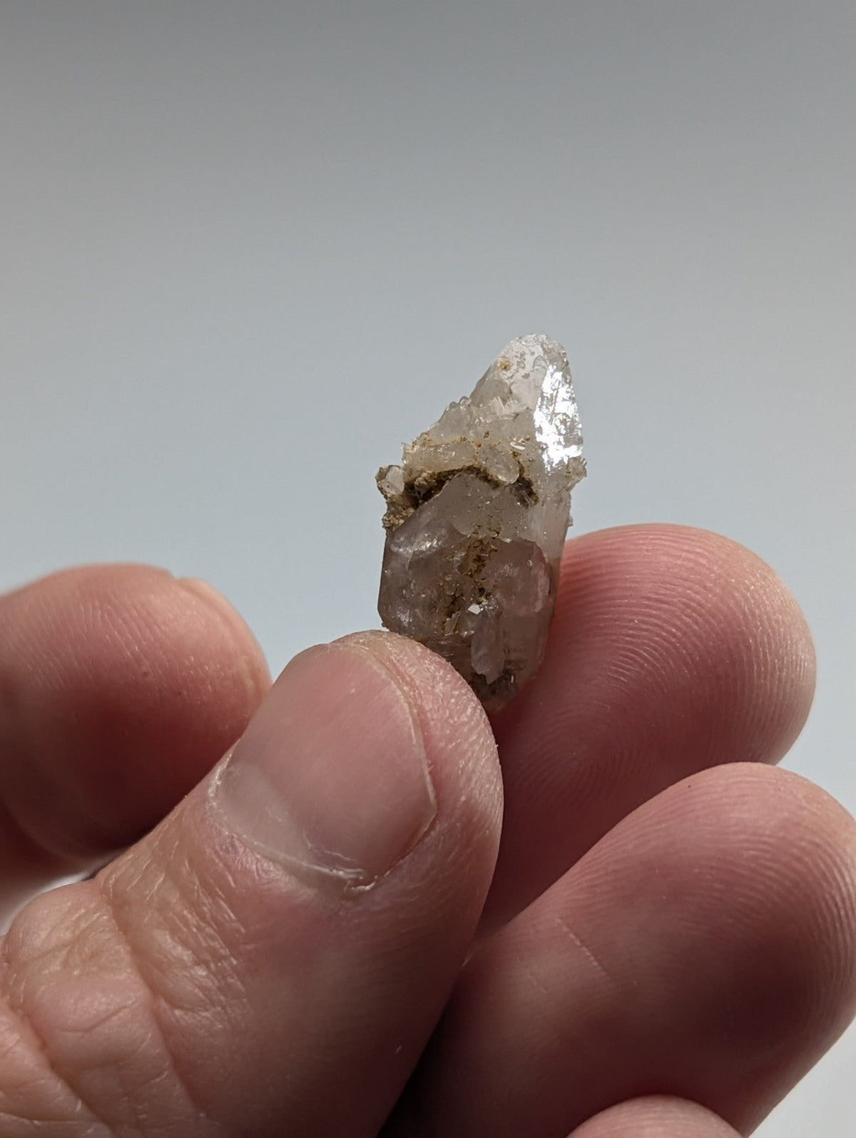 A translucent, pointed quartz crystal with a rough, earthy base and subtle golden inclusions.