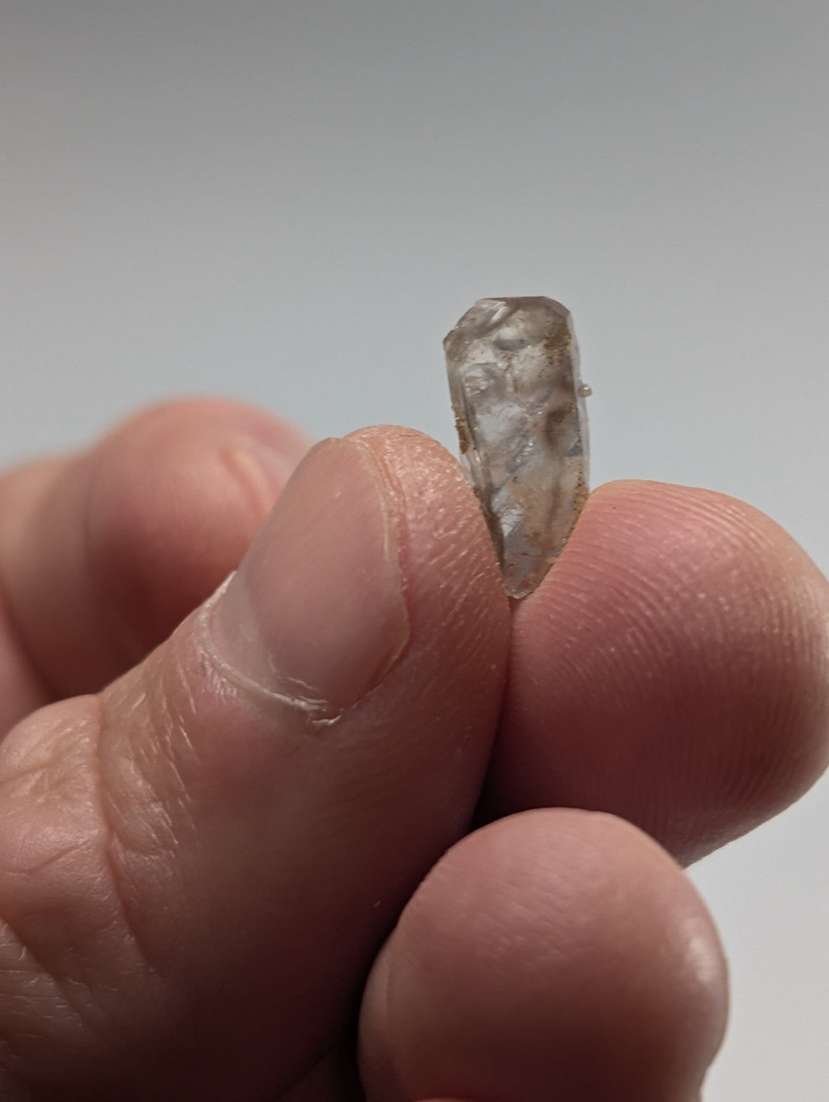 A translucent, rough-cut raw crystal held delicately between fingers.