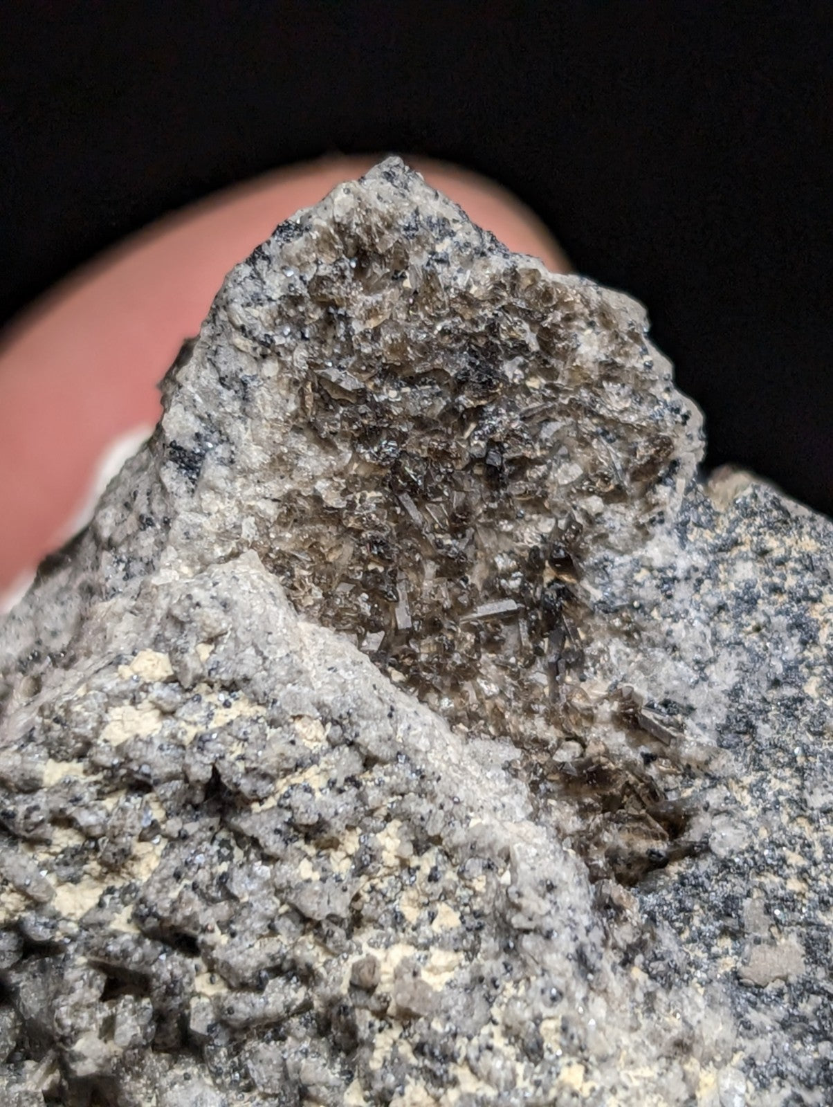 A rugged, grayish-black mineral specimen with a rough, crystalline texture and embedded translucent crystals.