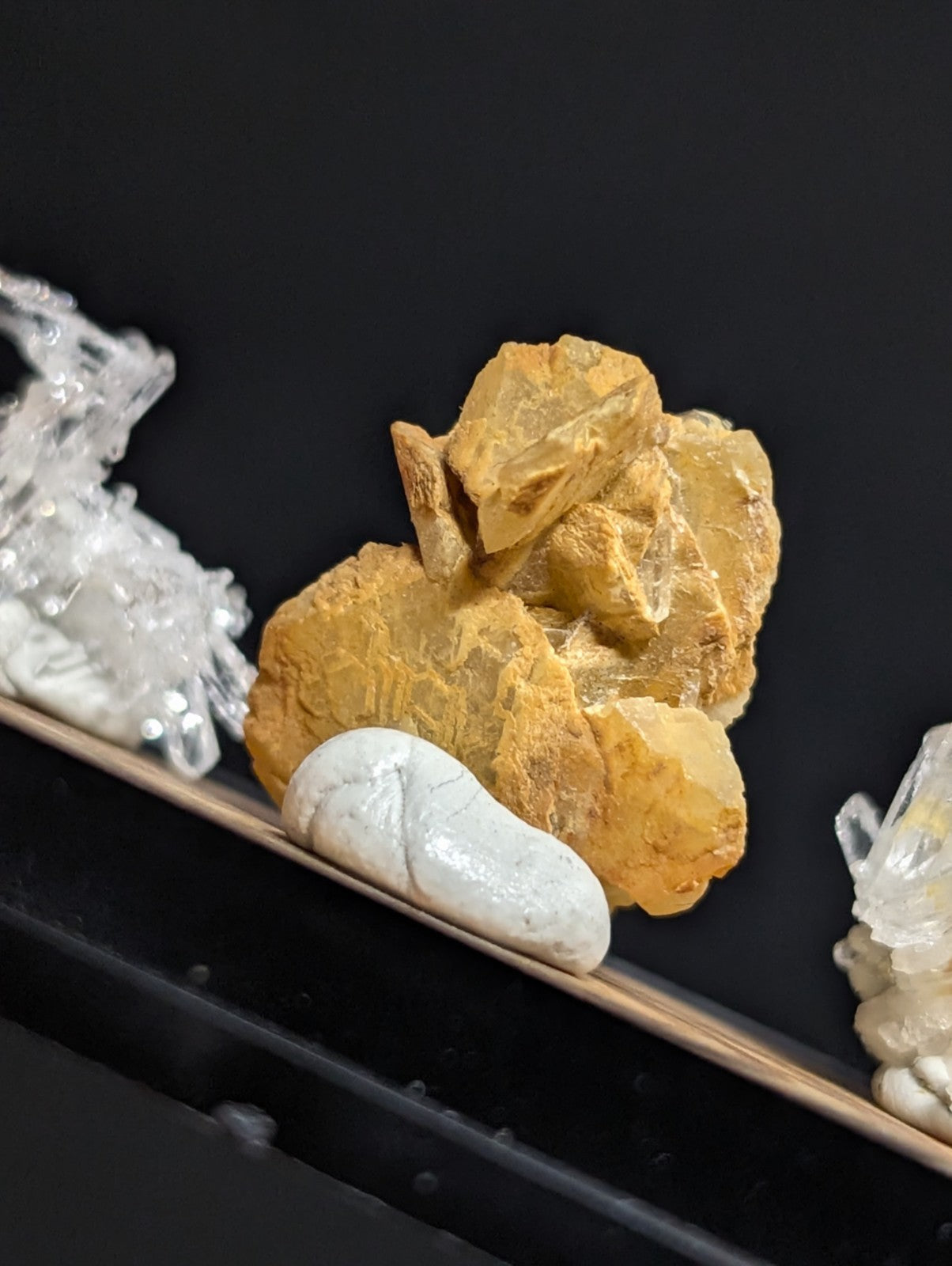 Golden-yellow mineral specimen with jagged, crystalline edges and a smooth white stone nestled in front.